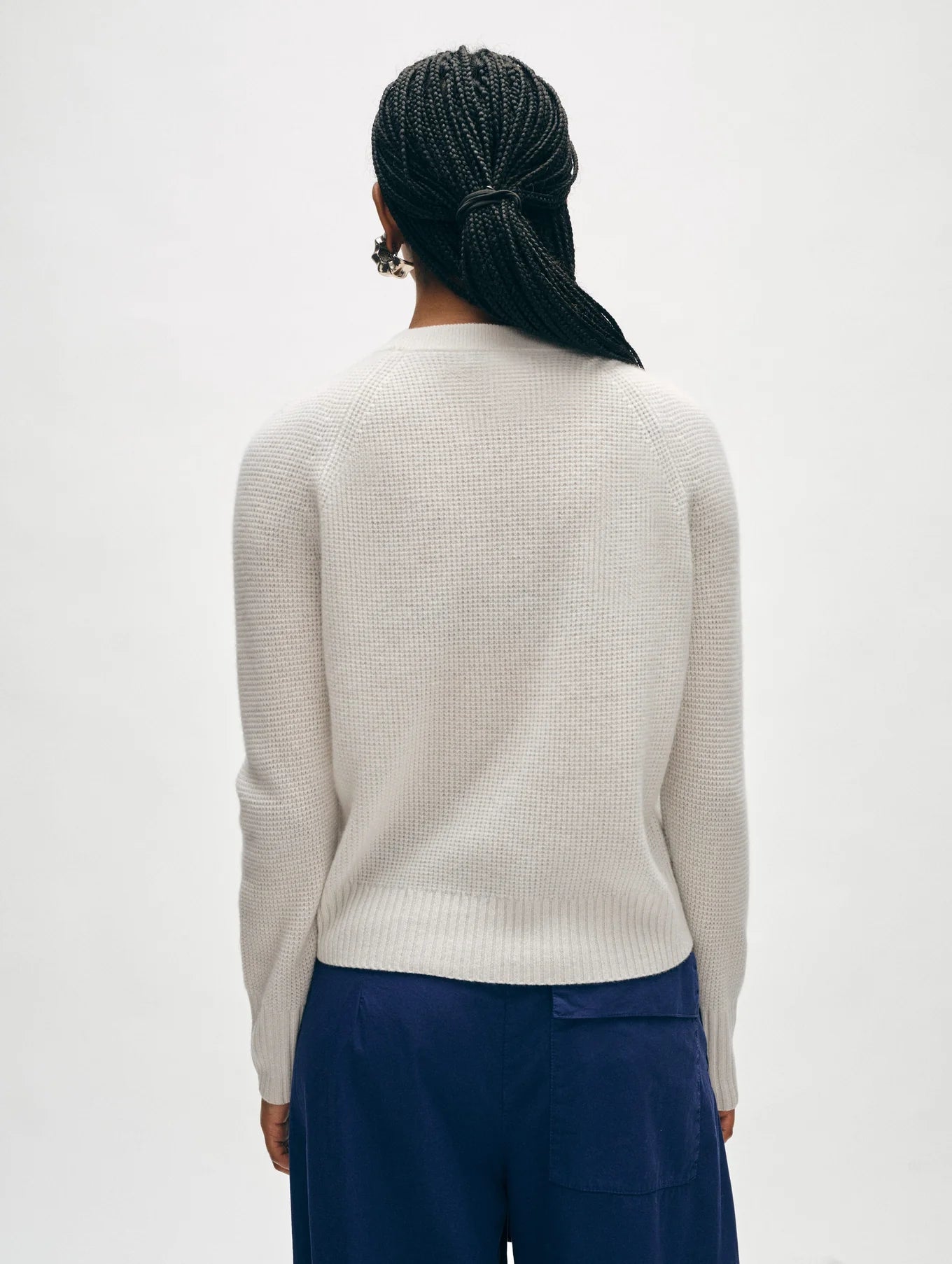 A person with braided hair is depicted from behind, wearing a light gray Cashmere Waffle Sweatshirt by White + Warren featuring a relaxed fit, along with dark blue pants set against a plain background.