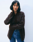 A woman with short black hair wears the White + Warren Cashmere Plaid Shacket with blue jeans, standing against a plain light background. She touches her neck and looks confidently at the camera.