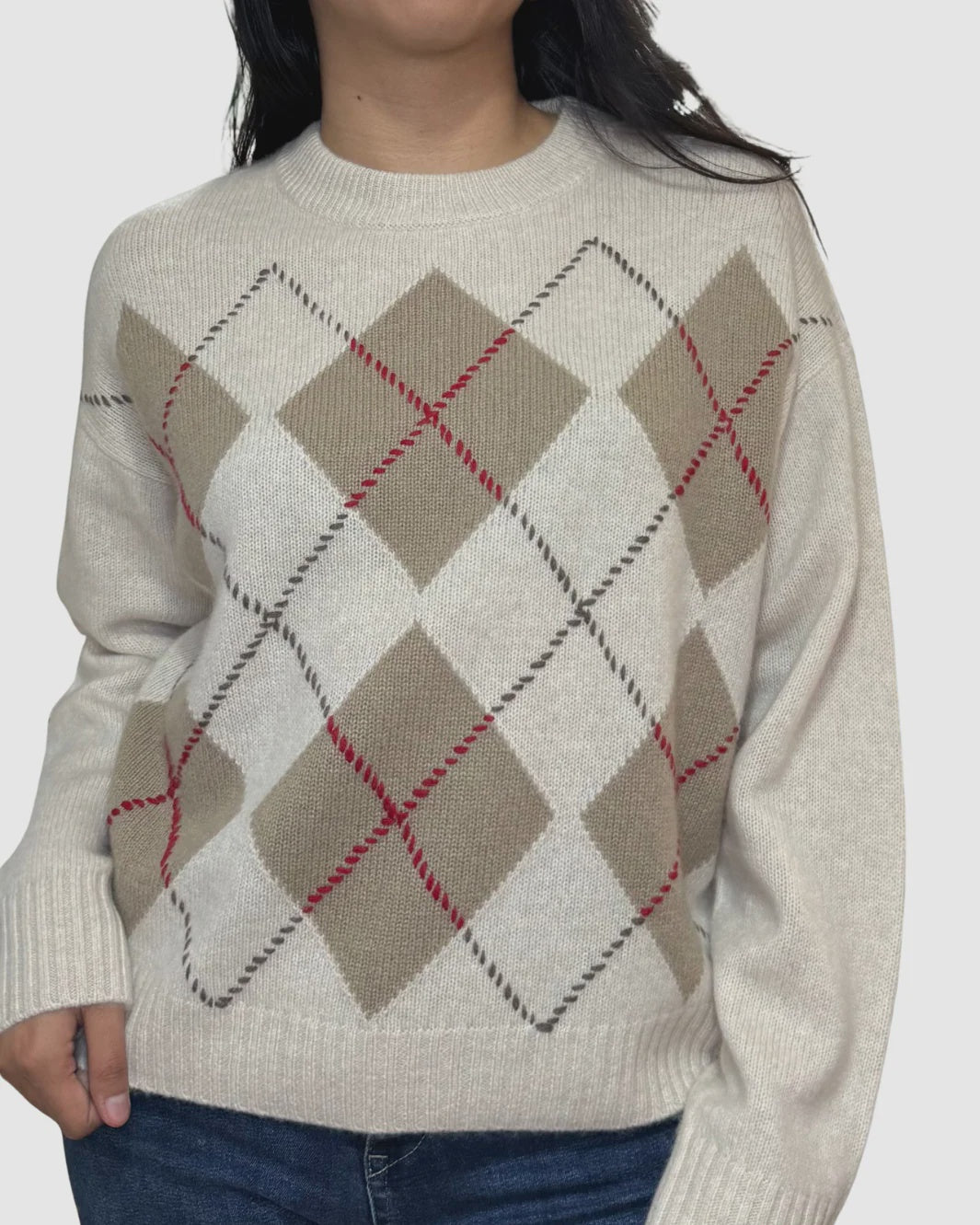 A woman wears the White + Warren Cashmere Argyle Crew in cream with beige, brown, and red accents, paired with blue jeans. The sweater has a round neckline and long sleeves, shown against a plain white background.