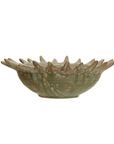 The Sunburst Serving Bowl by Creative Co-op is a handcrafted stoneware piece with a distinctive sunburst shape. It features upward-pointing spikes around the rim, resembling a stylized flower. The bowl is glazed in earthy tones of green and brown, enhanced with an opal reactive glaze for a rustic, artisanal appearance.