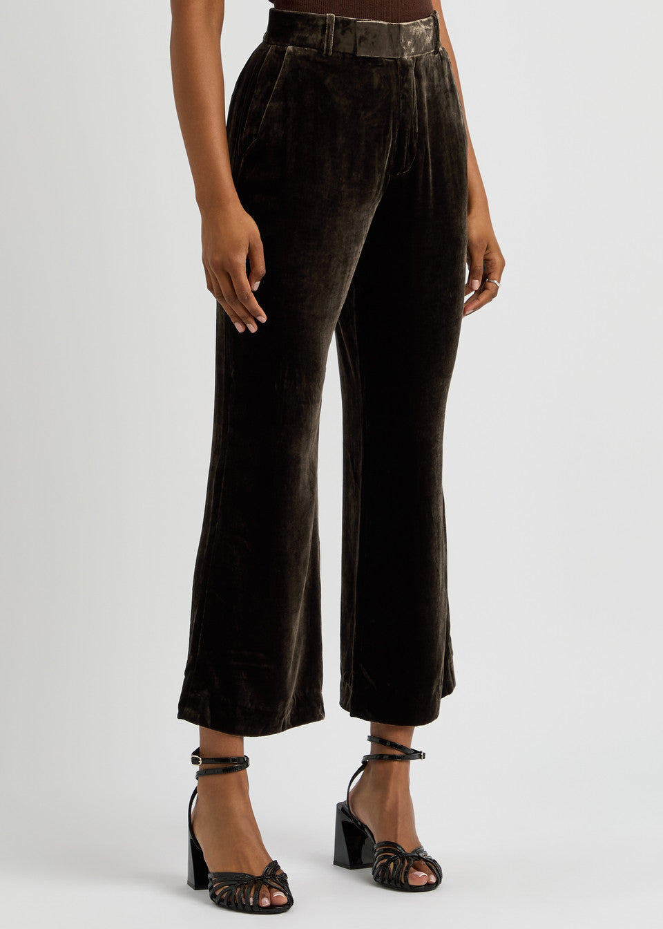 A person showcases the Crop Flare Velvet Trouser by FRAME, paired with black strappy heels. The focus is on the lower half against a plain background, accentuating the luxurious drape of the midweight fabric.