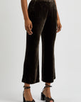 A person showcases the Crop Flare Velvet Trouser by FRAME, paired with black strappy heels. The focus is on the lower half against a plain background, accentuating the luxurious drape of the midweight fabric.