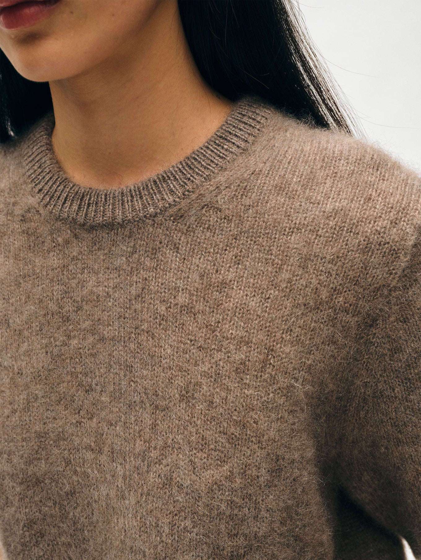 Close-up of a person wearing the Brushed Cashmere Tee by White + Warren. The image focuses on the upper torso and left side of the face, with long dark hair partially visible. The background is blurred, highlighting the texture and luxurious comfort of the tee.