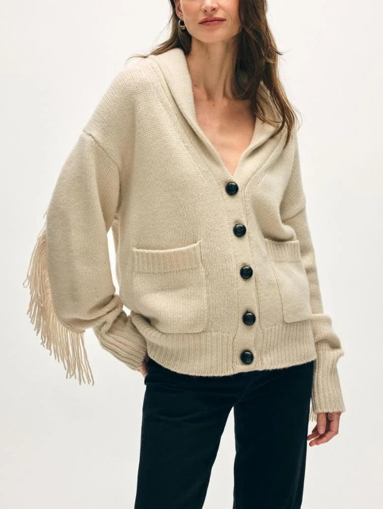 A woman models the White + Warren Cashmere Blend Luxe Fringe Coatigan, a cream-colored piece with black buttons, front pockets, and long fringed sleeves, styled with black pants against a plain light background.