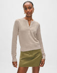 A woman with short hair and hoop earrings wears a White + Warren Fine Cotton Blend Henley sweater and an olive green mini skirt against a plain background, embodying versatile staple style with refined sophistication.
