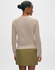 A woman with her hair in a bun is shown from behind, wearing the White + Warren Fine Cotton Blend Henley in light beige and an olive green skirt against a plain light background.