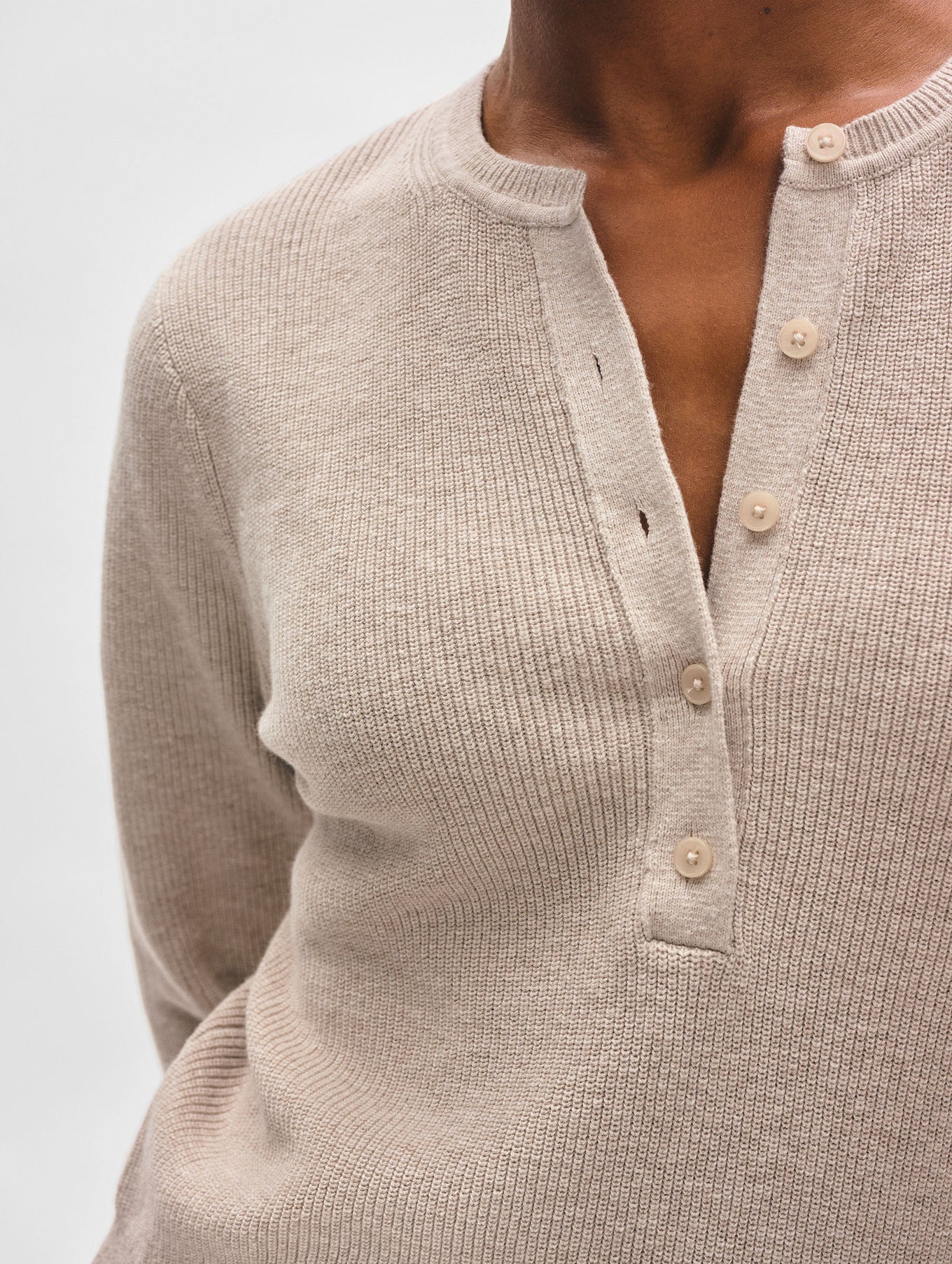 A close-up of a person wearing White + Warren’s Fine Cotton Blend Henley, a long-sleeve top with a button-front neckline left partially open, shown against a plain light background to highlight this versatile essential.