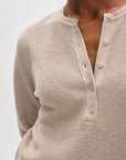 A close-up of a person wearing White + Warren’s Fine Cotton Blend Henley, a long-sleeve top with a button-front neckline left partially open, shown against a plain light background to highlight this versatile essential.