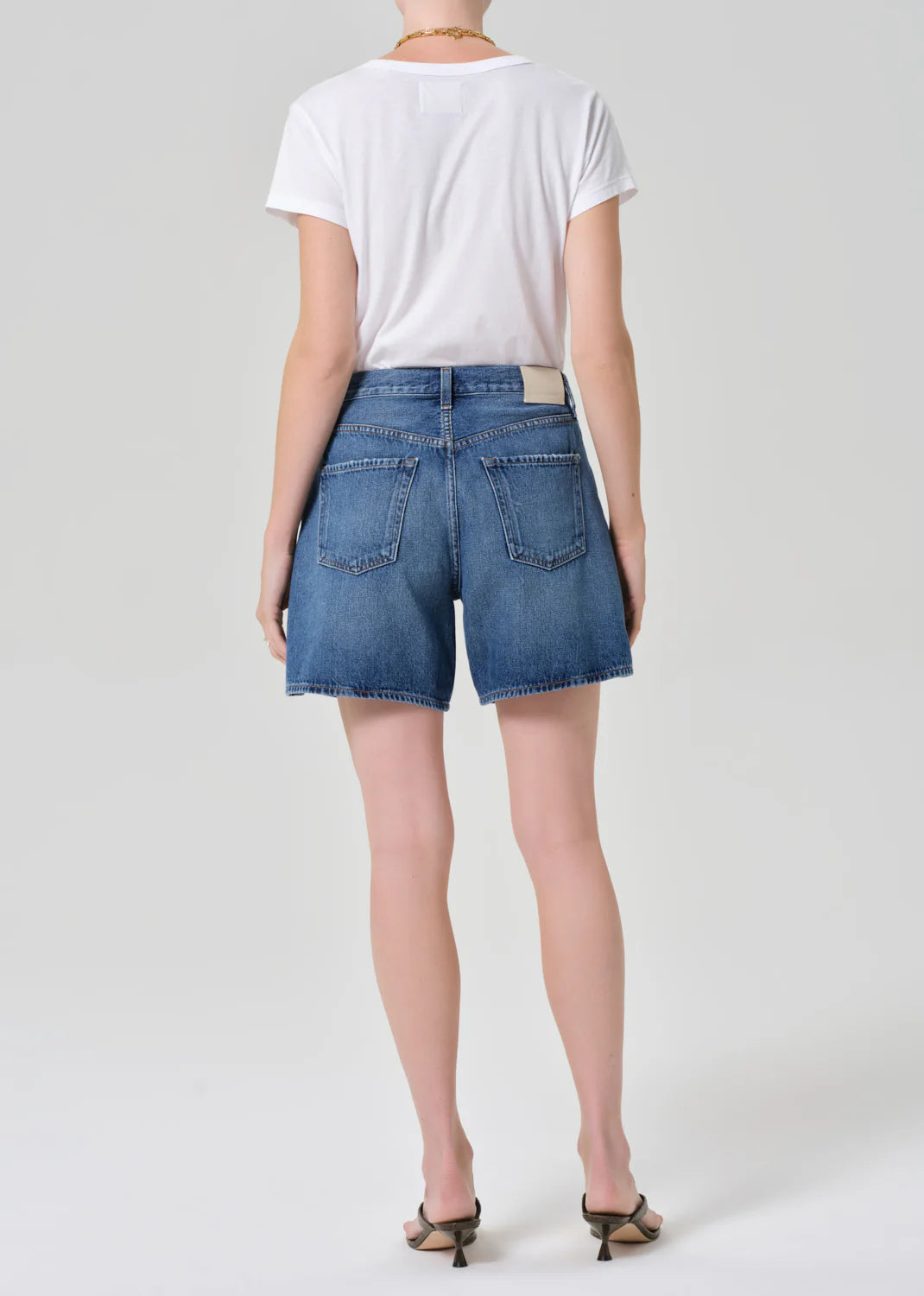 A person stands facing away against a plain light background, wearing a white t-shirt, heeled sandals, a gold chain necklace, and the Citizens Of Humanity/AGOLDE brynn drawstring short in avant (lightwt vintage).