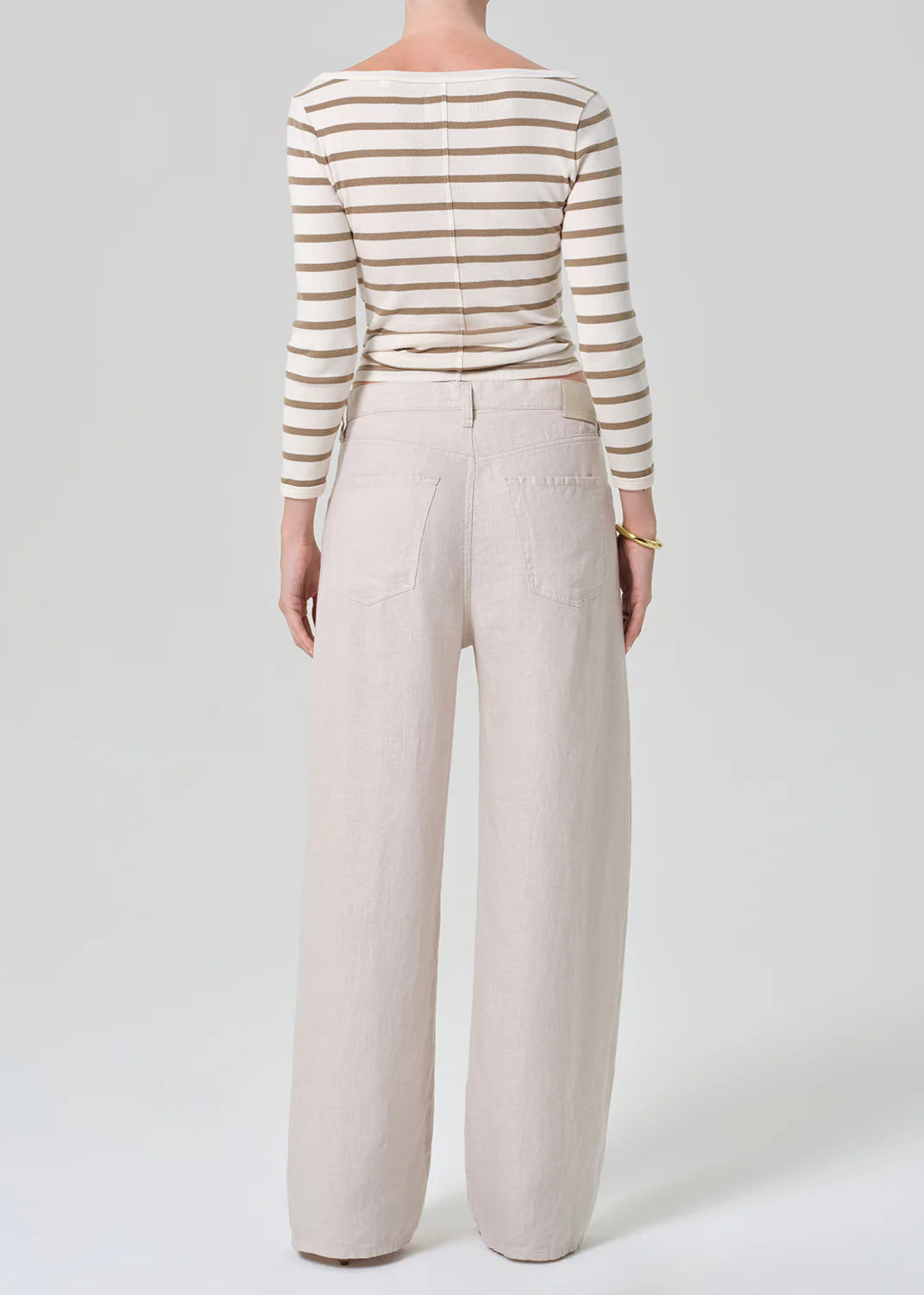 A person stands facing away, wearing a brown-and-white striped long-sleeve shirt and the brynn drawstring trouser in linen by Citizens Of Humanity/AGOLDE, set against a plain light background.