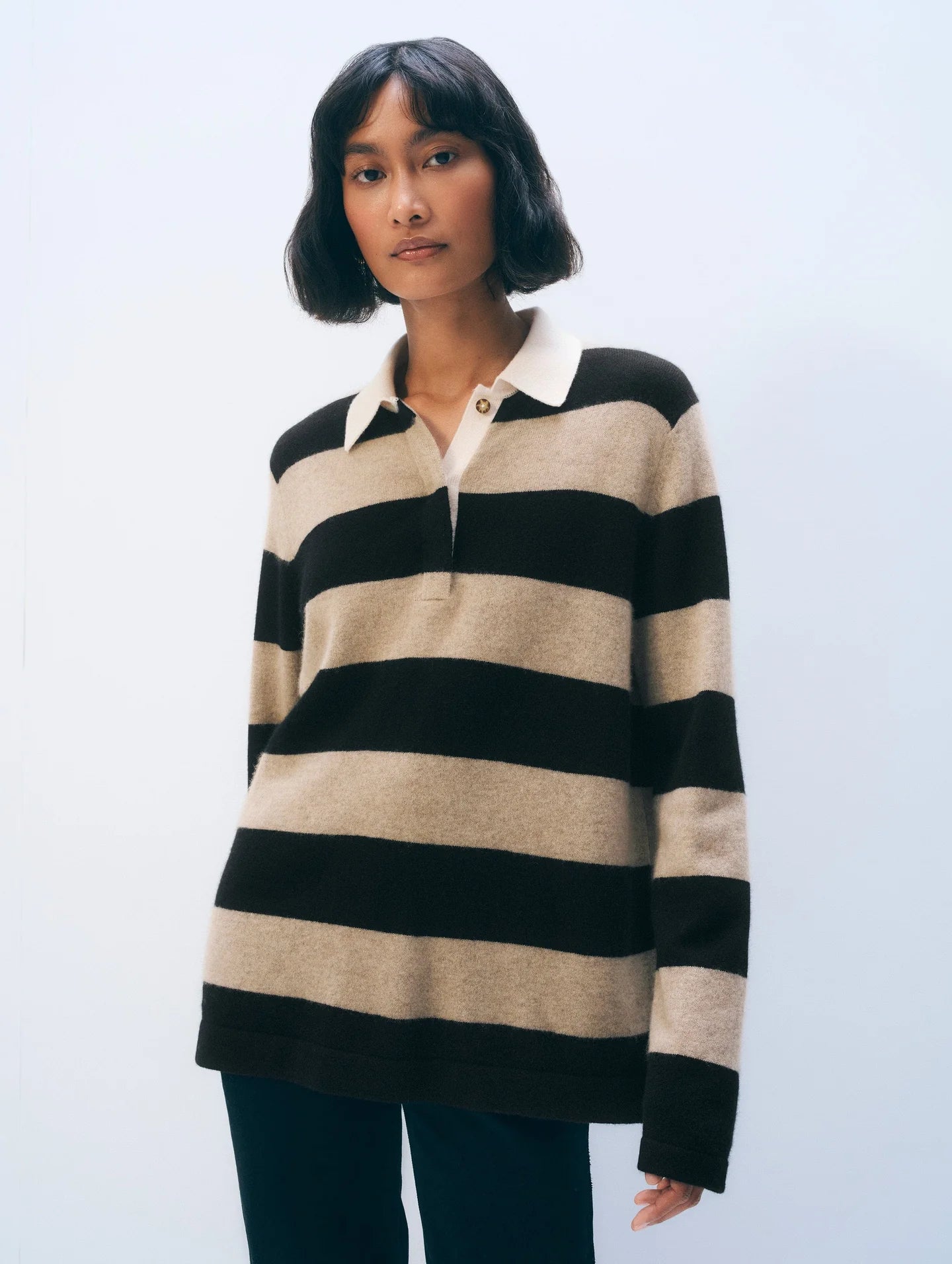 A woman with a short bob wears the White + Warren Cashmere Rugby Stripe Polo in beige and brown stripes with dark pants, standing against a light background.