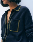 A person with a short, wavy bob wears the White + Warren Cashmere Tipped Button Shirt—a menswear-inspired dark blue cardigan with lime green trim at the collar, pocket, and front opening. The image is cropped at the shoulder and mouth.