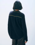 A person with short, wavy dark hair stands with their back to the camera, wearing the White + Warren Cashmere Tipped Button Shirt— a menswear-inspired, loose-fitting long-sleeve sweater with a horizontal stripe—paired with dark pants.