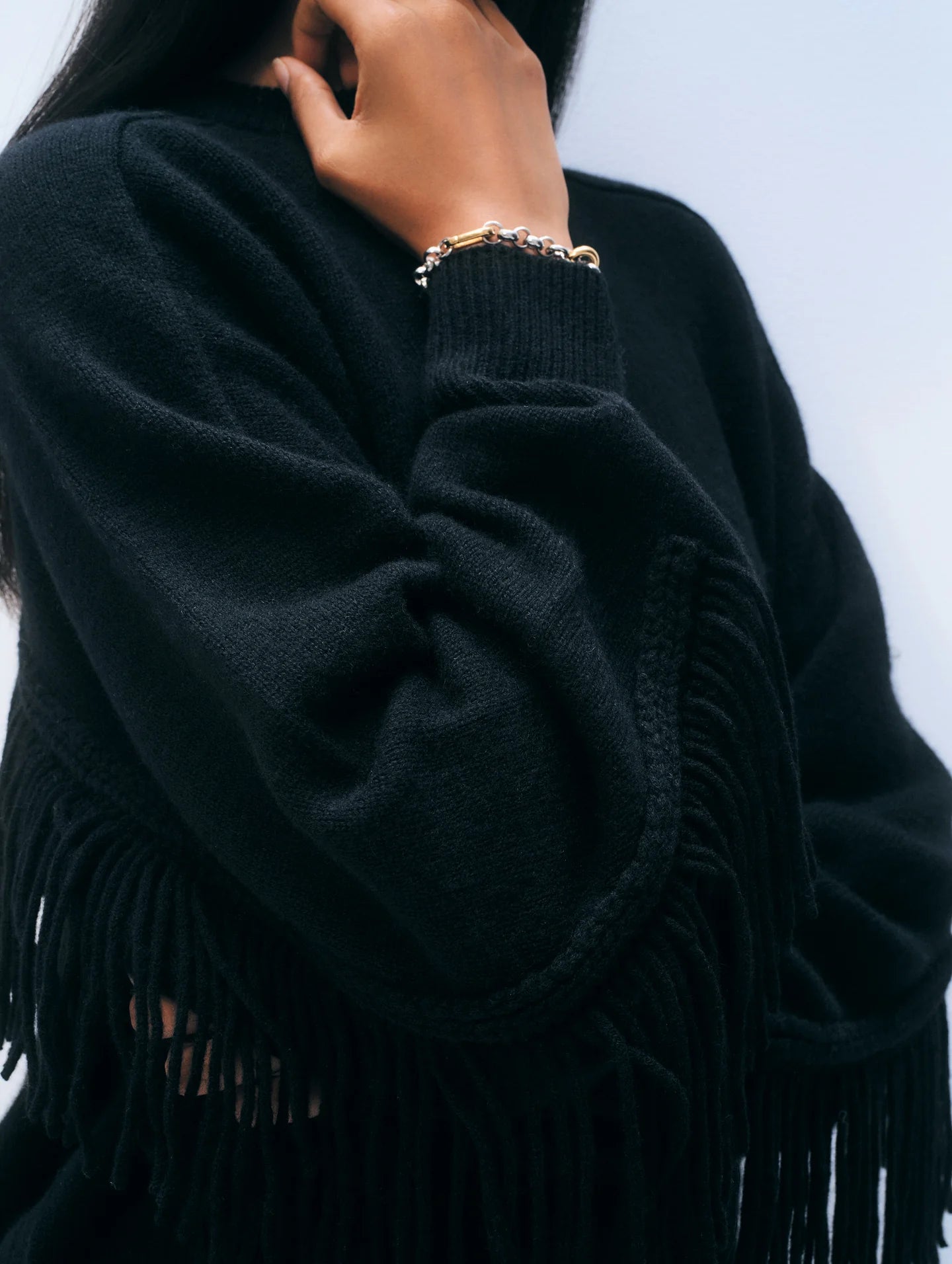 A person wearing the White + Warren Cashmere Luxe Fringe Crew, featuring long fringe on the sleeves and body, holds their hand by their chin to showcase a delicate beaded bracelet.
