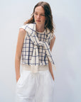 A woman with wavy brown hair wears the White + Warren Cashmere Windowpane Vest and a matching sweater over her shoulders, paired with white pants, standing against a plain light background.