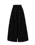 The Psophia Palazzo Wide Leg Trouser features a high-waisted, wide-leg silhouette and a textured floral jacquard pattern in black, embodying minimalist style and shown against a white background.
