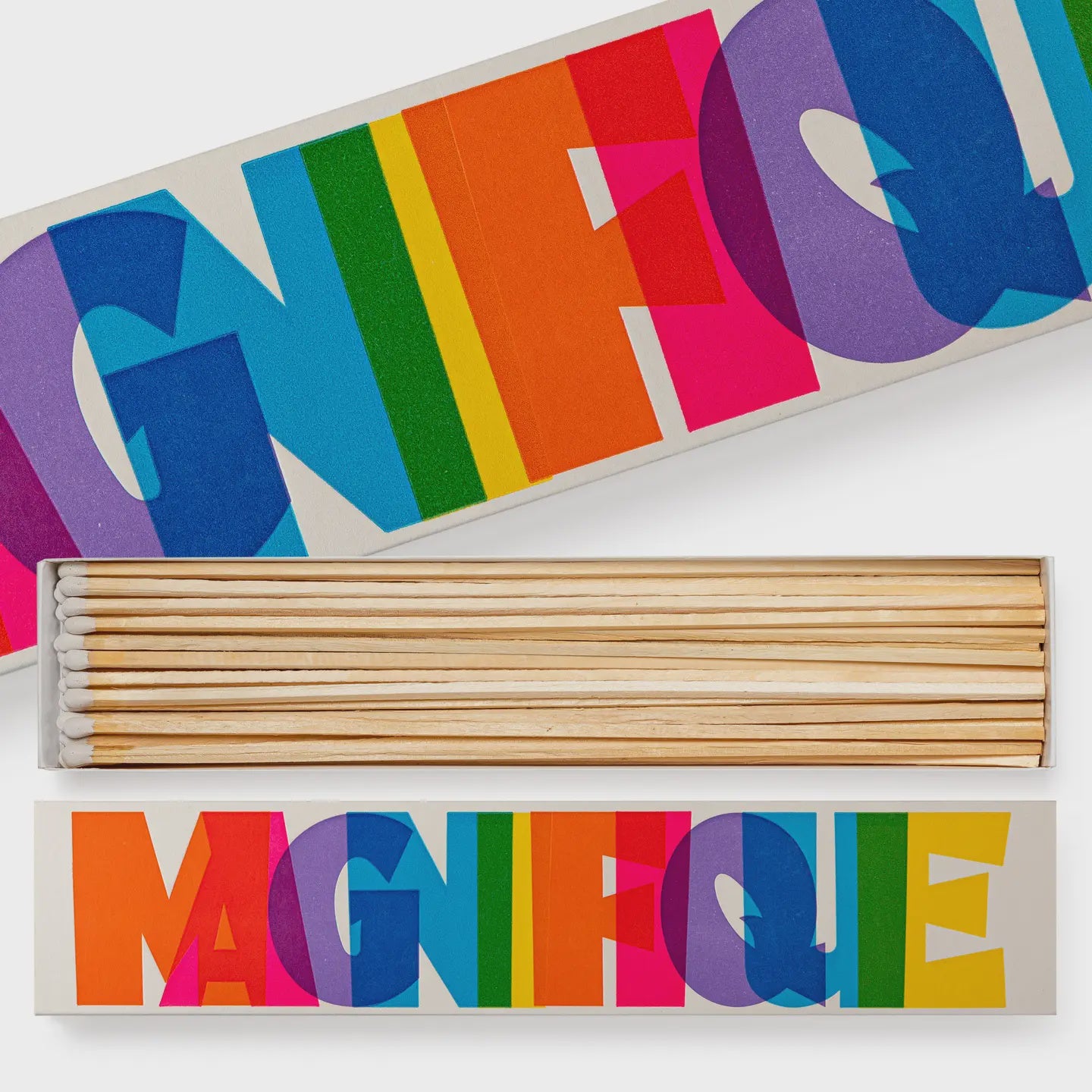 A box of Long Fireplace Matches by Faire showcases a vibrant "MAGNIFIQUE" design on the lid, with overlapping colors like blue, green, orange, pink, and purple. The open box reveals the long matches inside.