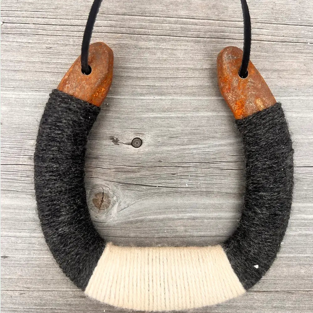 The Faire Lucky Horseshoe features rustic, rusty metal ends and is wrapped in black, gray, and white yarn. Hung on a black cord, it makes perfect upcycled home decor for a cozy touch.