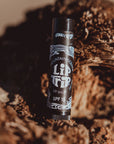A black tube of Faire Lip Trip SPF stands upright on a textured brown surface, softly lit by sunlight for outdoor lip protection.