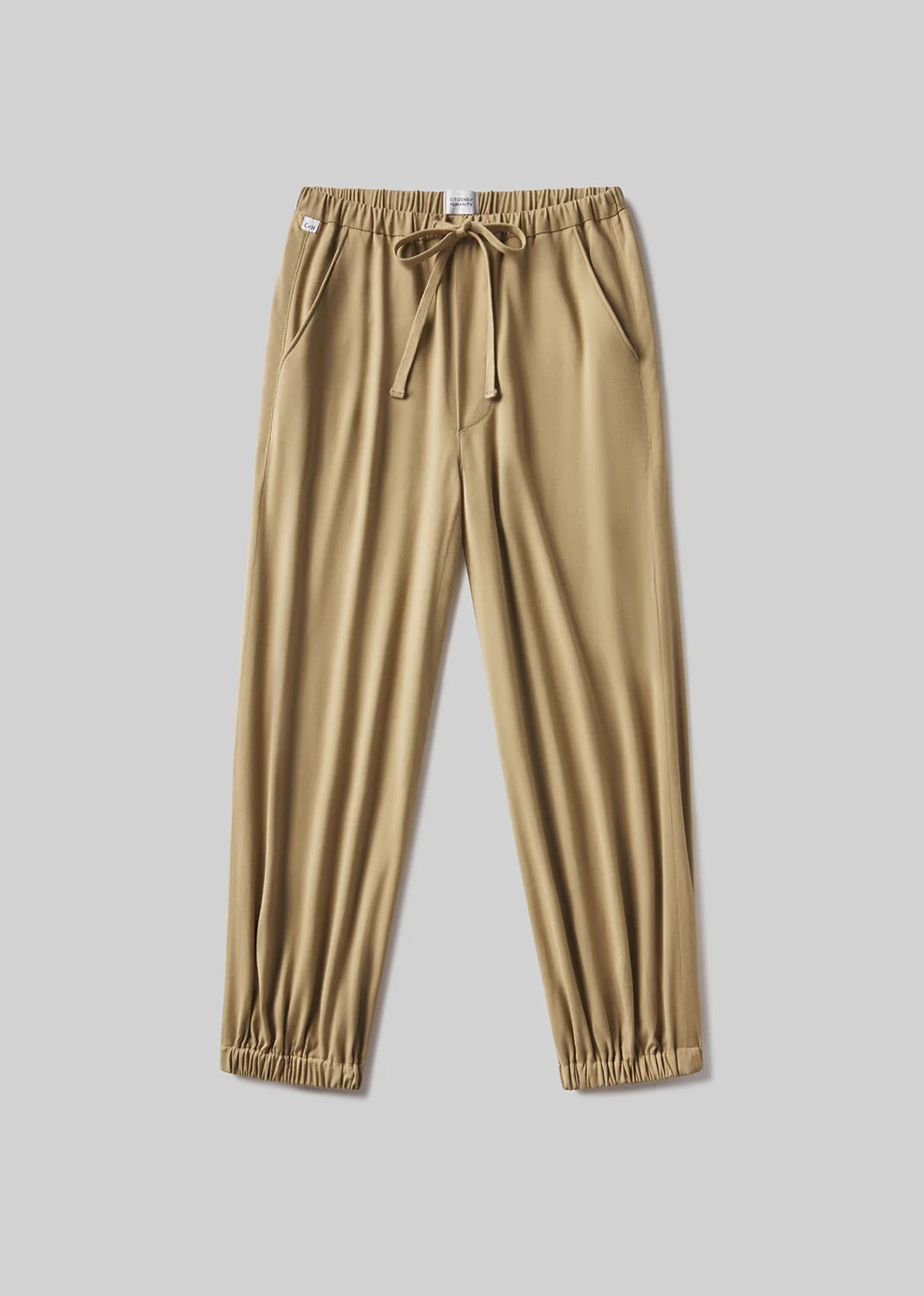 The Citizens Of Humanity/AGOLDE bubble pull on in portofino twill pants, tan-colored and lightweight, feature an elastic waistband with a drawstring tie, side pockets, and elastic cuffs. Shown laid flat on a light gray background.