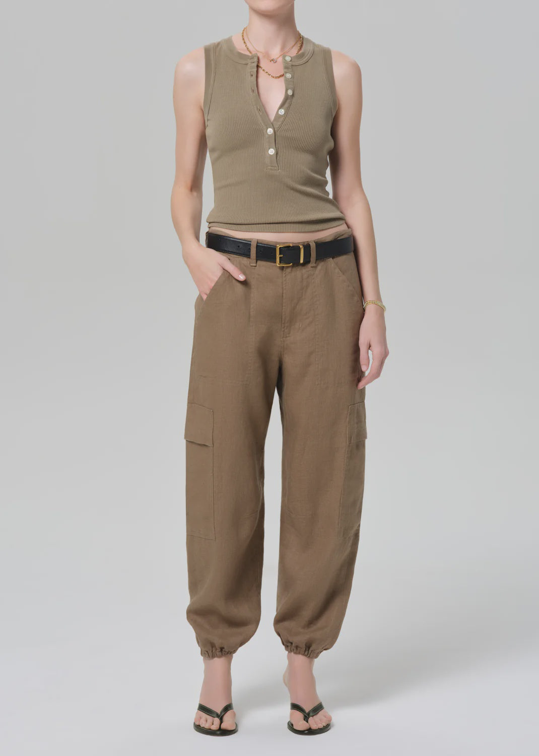 A person wearing Citizens Of Humanity/AGOLDE's ciela balloon utility brown cargo pants with a utility-inspired silhouette, styled with a sleeveless ribbed tank, black belt, gold jewelry, and sandals against a plain light background.