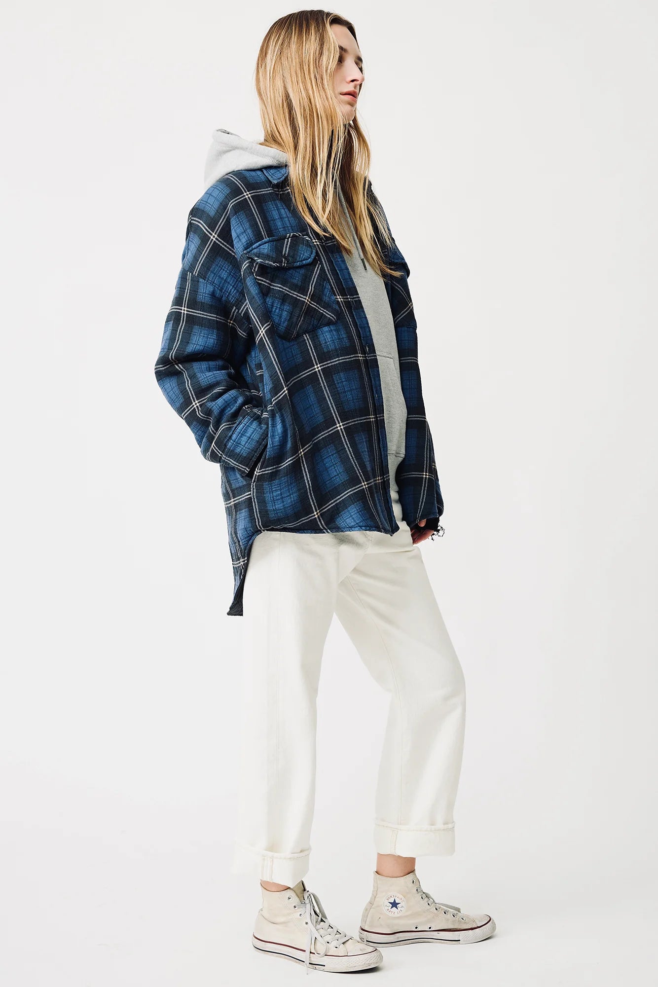 A person with long hair wears a blue and black Denimist CPO SHIRT JACKET over a gray hoodie, white cuffed cotton pants, and light-colored Converse sneakers, standing against a plain white background.