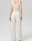 A person faces away from the camera, wearing Citizens Of Humanity/AGOLDE's aurora track pant in off white with black side piping and a back pocket, made from an Italian cotton blend, paired with a sleeveless ribbed white tank top.