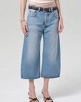 Wearing the Citizens Of Humanity/AGOLDE vintage culotte in sunlit, paired with a brown belt, sleeveless striped top, and black heeled sandals, this person stands against a plain light background.