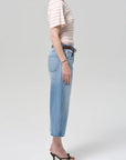 A person stands in profile against a plain background, wearing a short-sleeve striped shirt, Citizens Of Humanity/AGOLDE vintage culotte in sunlit, and black heeled sandals. Their face is not visible.