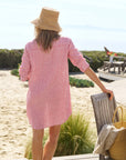A woman in the Frank & Eileen MARY Shirtdress S25 and a straw hat stands on the beach, holding a wooden chair with a woven bag and towel—capturing effortless seaside style.