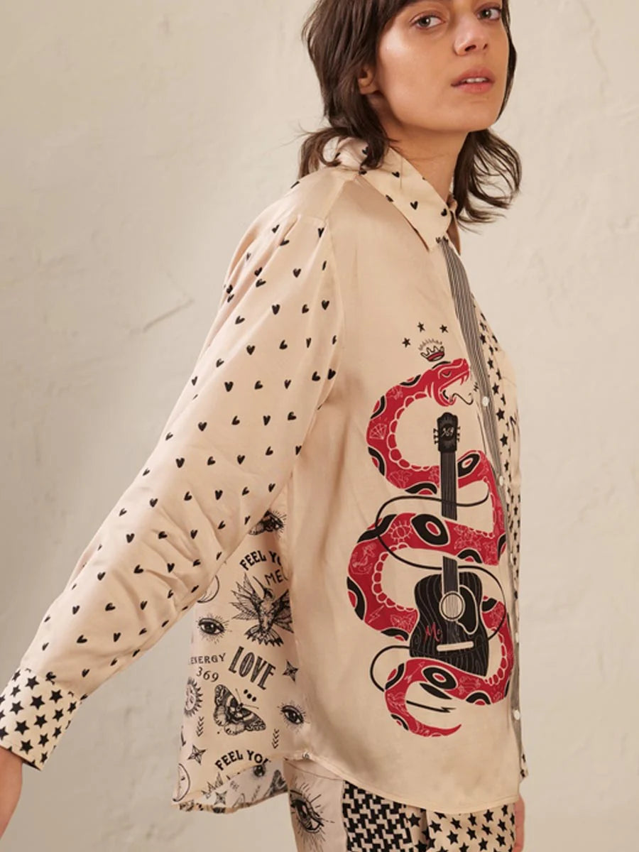A person wearing the Me369 Scarlett Print Shirt, made from 100% viscose, features mixed prints of black hearts, stars, and eyes with a bold red snake wrapped around a black guitar graphic on the side.