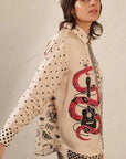A person wearing the Me369 Scarlett Print Shirt, made from 100% viscose, features mixed prints of black hearts, stars, and eyes with a bold red snake wrapped around a black guitar graphic on the side.