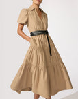 A woman models the HAVANA DRESS by BROCHU WALKER, a tan, short-sleeve, button-down dress with a tiered skirt and pockets. She stands against a light background, her waist cinched with a black belt.