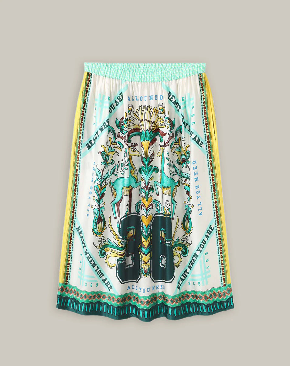 The Vanessa Midi Skirt by Me369 is a colorful viscose midi with an elastic waist, featuring green deer, floral motifs, ornate green, teal, yellow, and black borders, and decorative text on white. Pair with the matching shirt for a chic look.
