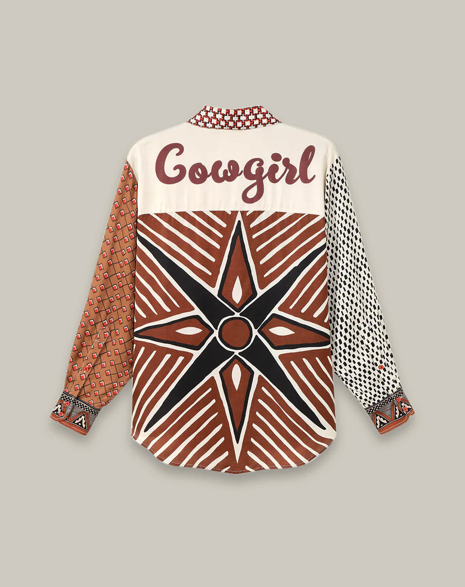 The Isabel Shirt by Me369 is a vintage-inspired long-sleeve top with mixed brown, cream, and black patterns. It features a bold "Cowgirl" script and large star on the back plus unique geometric sleeve details.