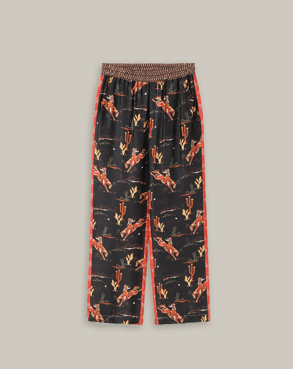 The Me369 Bailey Track Pant features a wide-leg, elastic waist and colorful cowboy, rodeo, and "IU" print on black with red side stripes—blending comfort and flair for standout style.