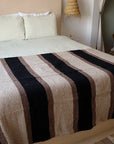Faire Blackstone Lines Handwoven Blanket on a bed in a cozy room with light pillows and straw lamps, Bungalow style.