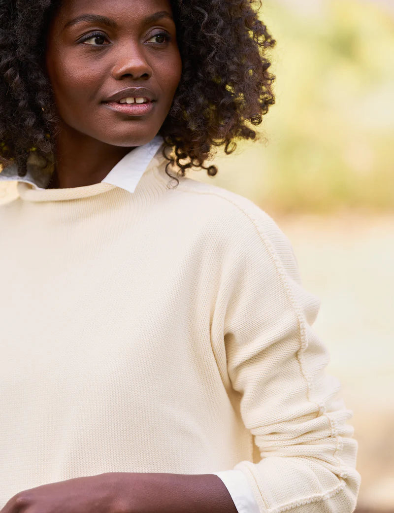 A person with curly hair is wearing the luxurious Monterey Sweater by Frank &amp; Eileen over a collared shirt, looking to the side. The background is softly blurred in a natural outdoor setting, creating an atmosphere of warmth and relaxation.