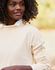 A person with curly hair is wearing the luxurious Monterey Sweater by Frank & Eileen over a collared shirt, looking to the side. The background is softly blurred in a natural outdoor setting, creating an atmosphere of warmth and relaxation.