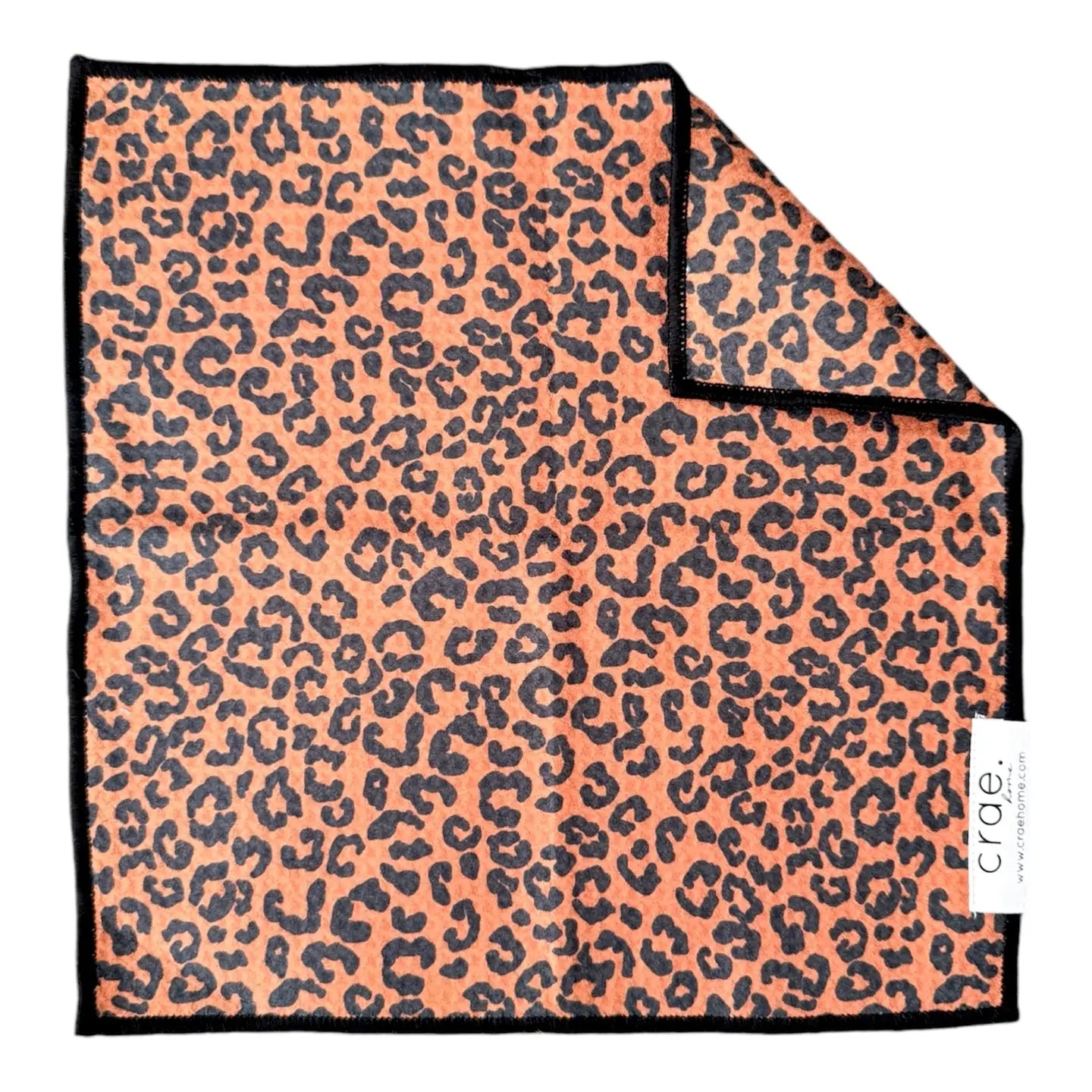 A square waffle weave microfiber washcloth from Faire features an orange and black leopard print, black edges, a folded corner showing the reverse, and an eco-friendly design. A white tag with the brand name "Faire" is attached.