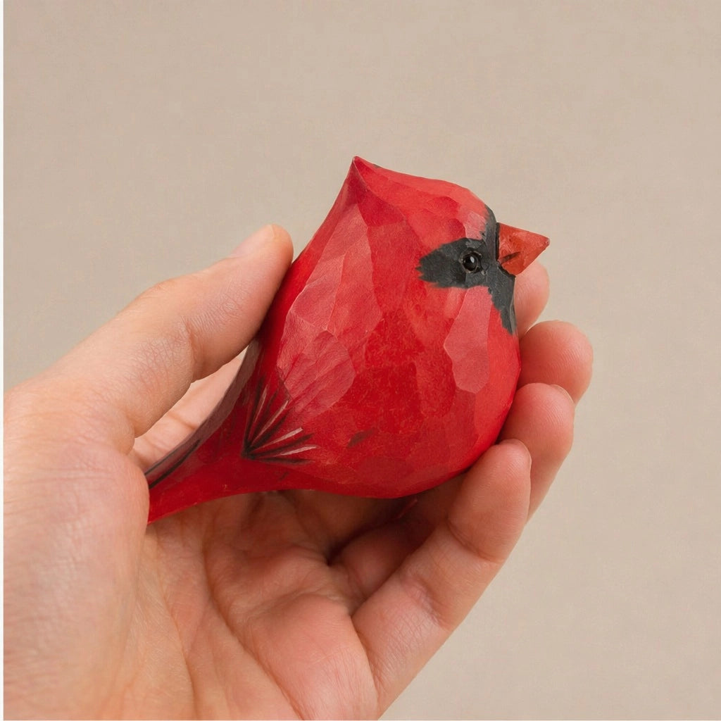 Red hand-painted wood bird figurine with black markings by Faire, held in a hand.