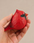 Red hand-painted wood bird figurine with black markings by Faire, held in a hand.