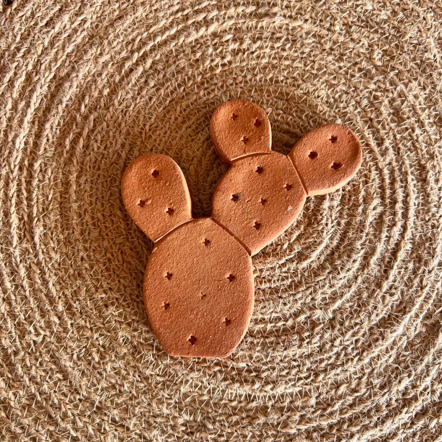 The Faire Brown Sugar Keeper is a handmade, cactus-shaped terra cotta ceramic ornament with small holes, placed on a round woven mat for a rustic, natural look reminiscent of traditional brown sugar storage.
