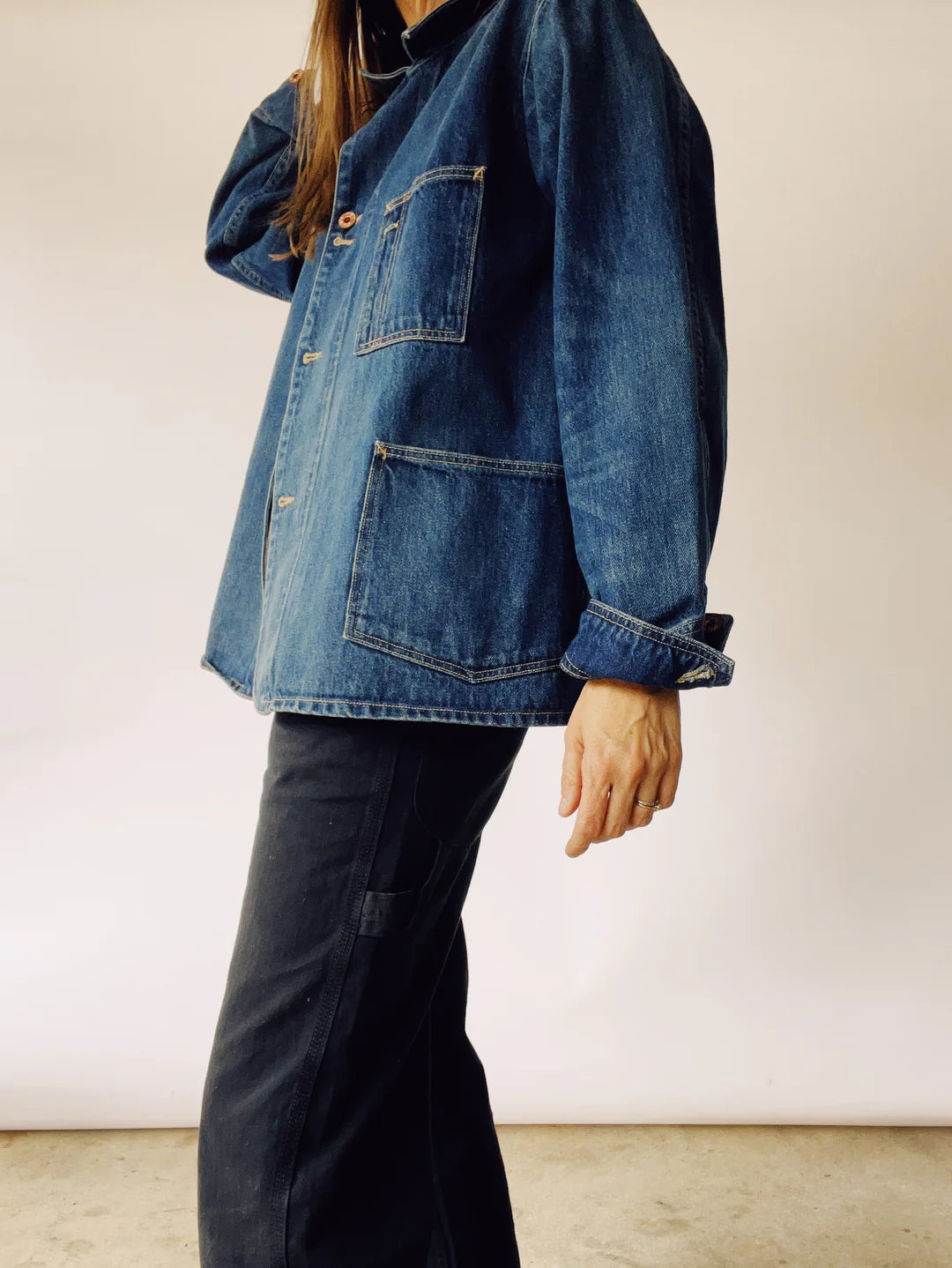 A person wearing The Barn Coat by Hey Gang and dark pants stands in front of a neutral background. The jacket, reminiscent of a chore coat with its large pockets, complements the casual and relaxed style as their right hand rests on their hip.