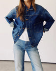 A person exudes confidence with hands on hips, wearing Hey Gang's "The Denim Jacket" along with jeans, standing against a plain white background.