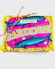 The Sardine Tin Luxury Soap by Faire is wrapped in red and white twine. The vibrant label, featuring blue fish illustrations, reads "Salted Lemon Sea Salted Sardines" with "Tinned in Lisbon, Portugal." Its bright yellow and magenta design resembles luxury soap bars.