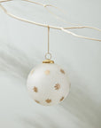 The North Star Ornament 6" by Accent Decor features frosted white glass with gold star patterns, ideal for gifting in a 6x6x6 box, and looks stunning hanging from a white branch against a light background.