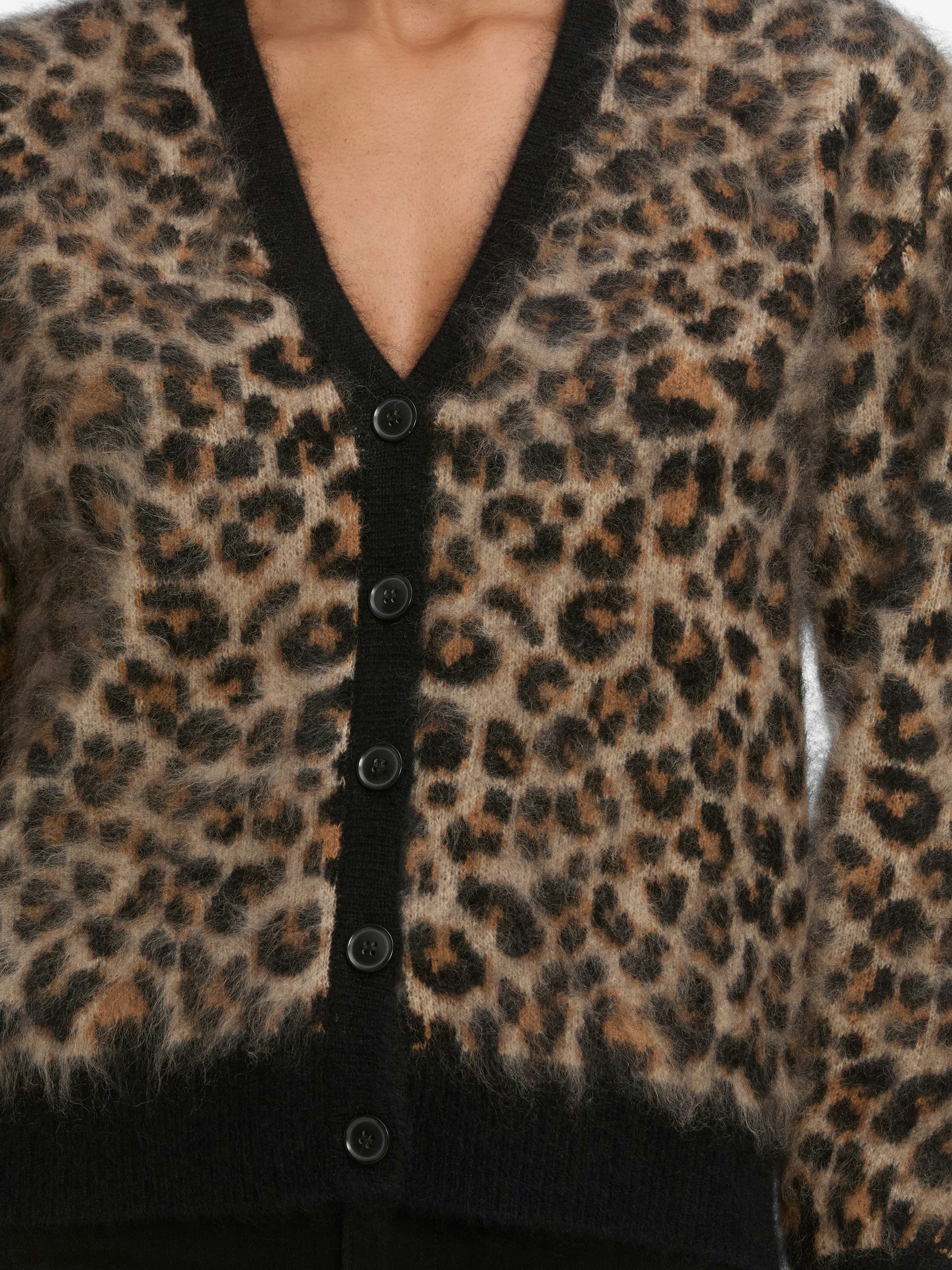 A person wears the FRAME Brushed Leopard Cardi, a statement cashmere cardigan with black buttons and a deep V-neck. The brown, tan, and black leopard pattern stands out. The photo is cropped at the chest and hips.