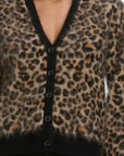 A person wears the FRAME Brushed Leopard Cardi, a statement cashmere cardigan with black buttons and a deep V-neck. The brown, tan, and black leopard pattern stands out. The photo is cropped at the chest and hips.