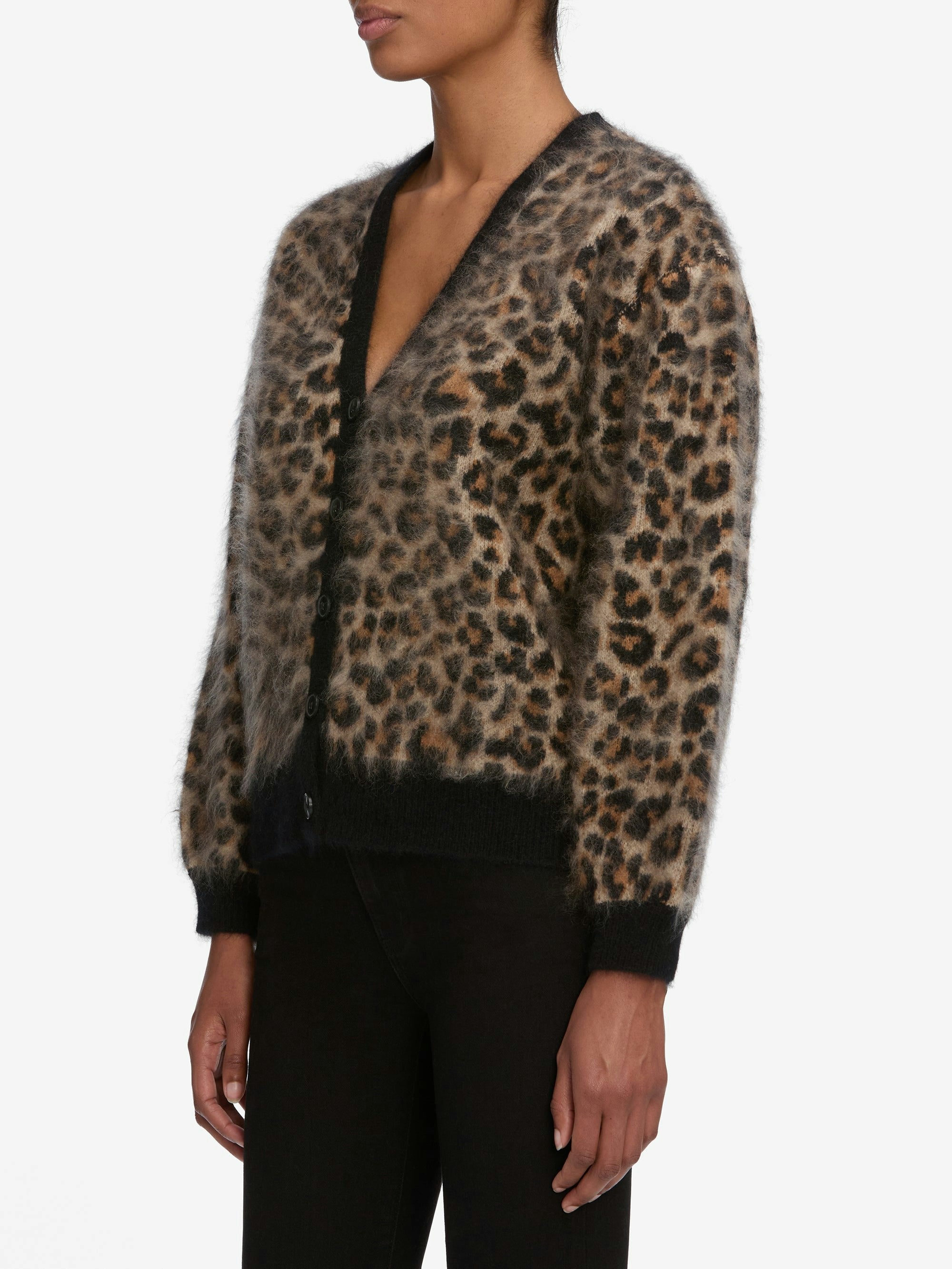A person wears the FRAME Brushed Leopard Cardi, a fuzzy leopard-print cardigan with black trim on the cuffs and hem, paired with black pants, against a plain white background.